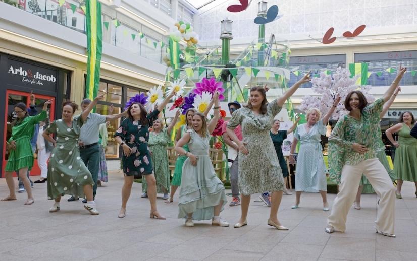 Performers from community chorus in a guildford shopping centre dancing together while wearing green and white outfits